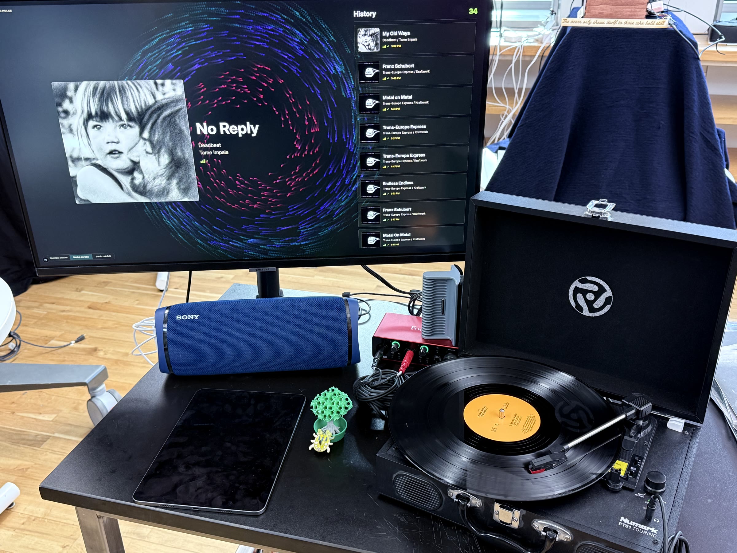 A turntable playing a record beside a monitor showing Collxn Pulse listening history.